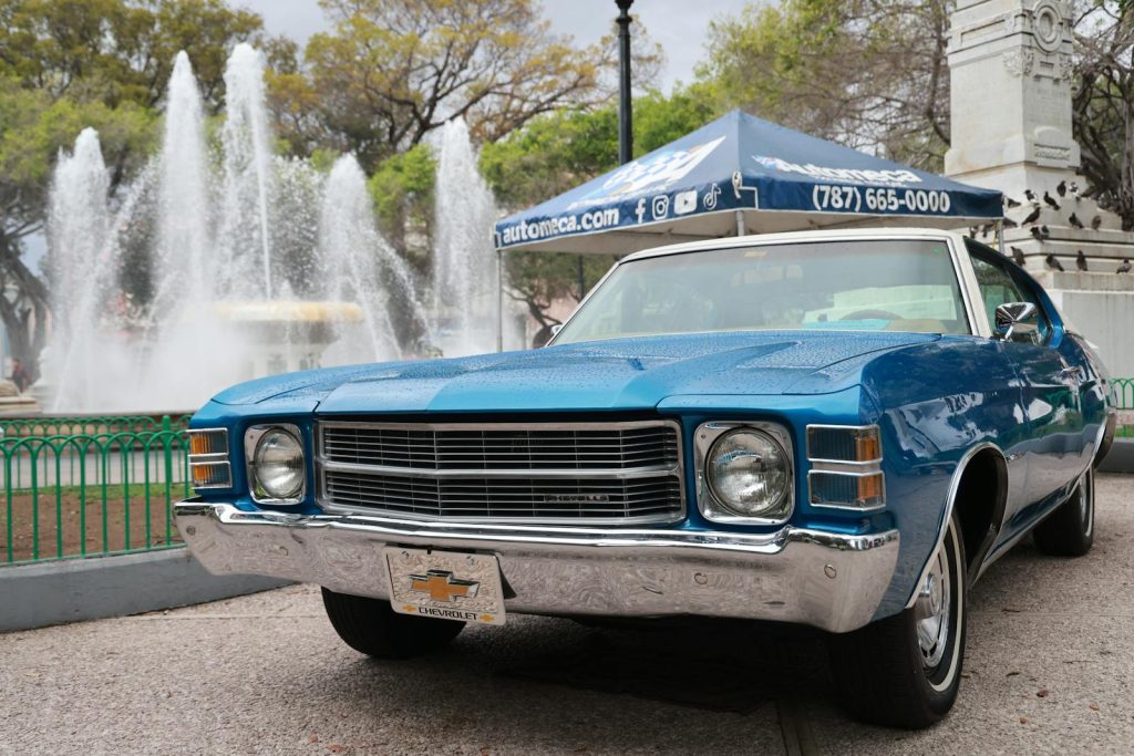 Vintage blue Chevrolet parked near a city fountain on a clear day.