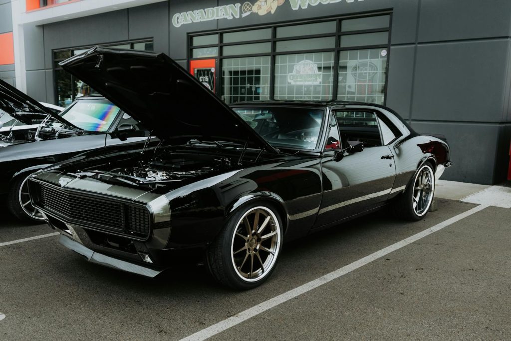 A shiny black classic muscle car with hood open displayed in an outdoor auto show.