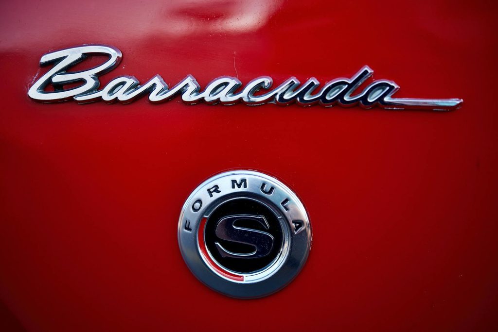 Close-up photo of classic Barracuda car emblem on a red vehicle, highlighting vintage style.