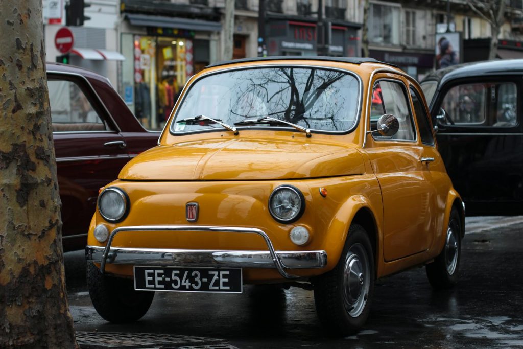 Classic yellow Fiat 500 parked in a bustling urban street, showcasing its retro style.