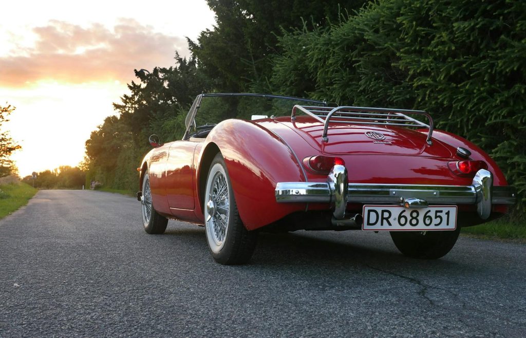 A classic red convertible parked on a scenic road at sunset, showcasing luxury and style.