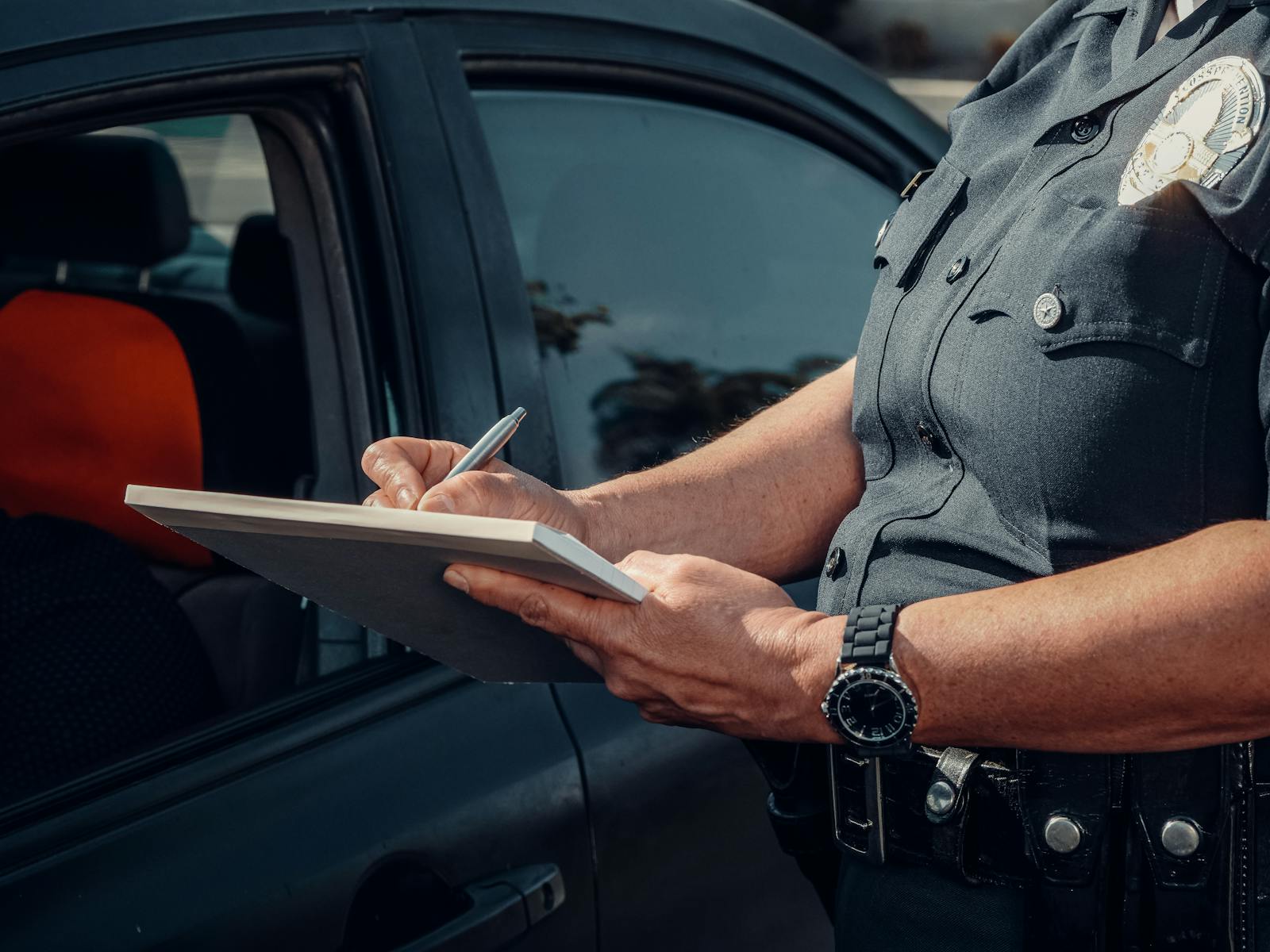 Close-up of a police officer writing a ticket by a car window. Law enforcement scene.