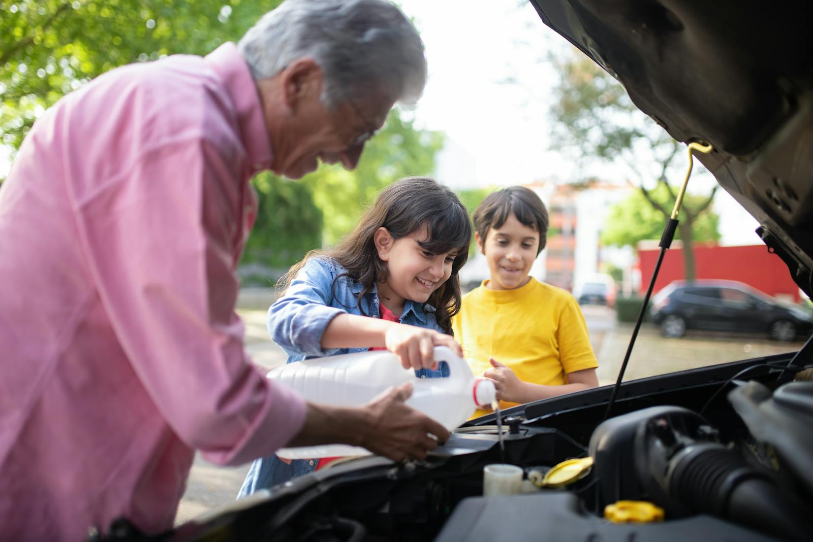 A grandfather and his grandchildren refilling car windshield fluid on a sunny day outdoors.