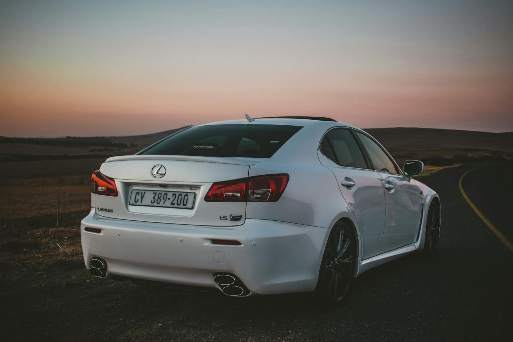 Stylish white Lexus IS parked on an empty road under a dramatic sunset sky.