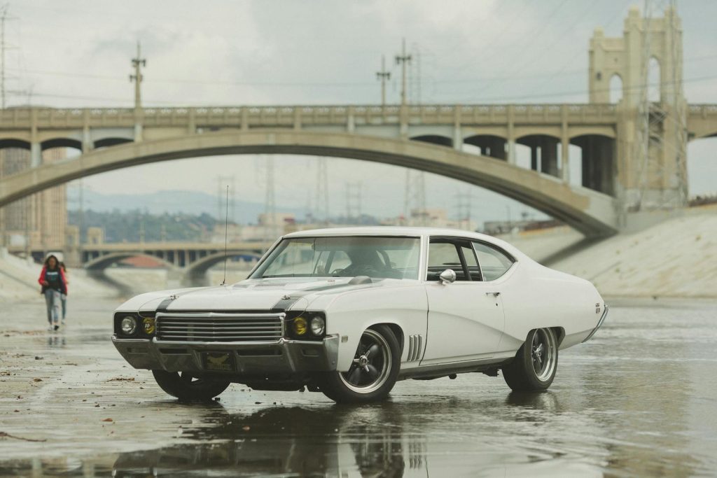 Classic white muscle car parked beside a bridge, showcasing vintage automotive design.