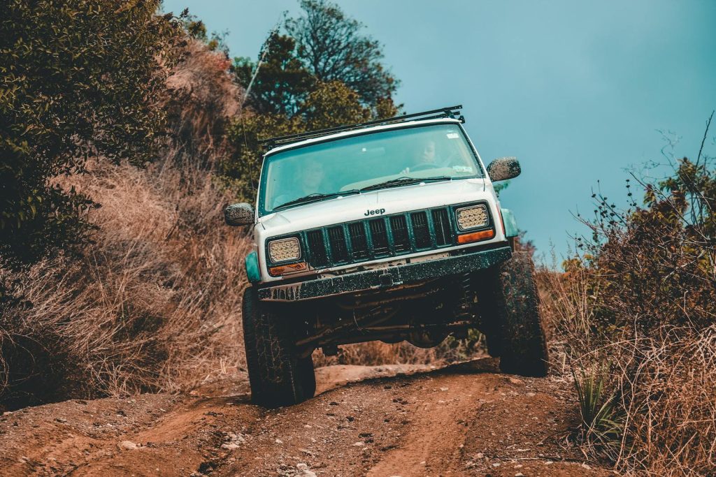 A rugged Jeep navigating a challenging muddy offroad trail through dense forest.