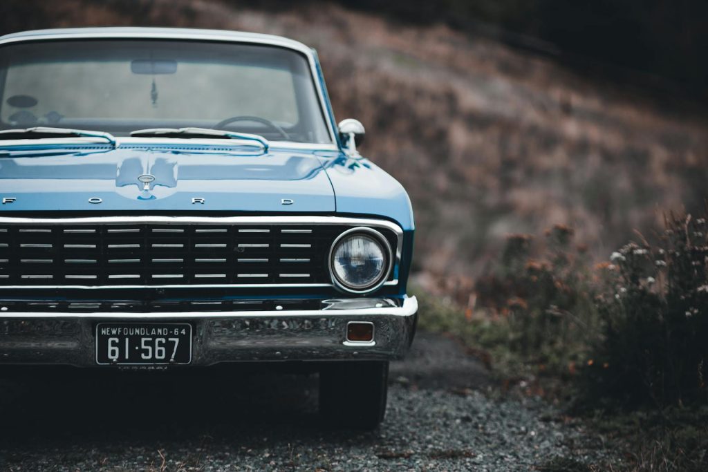 Close-up of a classic blue Ford Falcon with Newfoundland plate, parked along a rustic road.