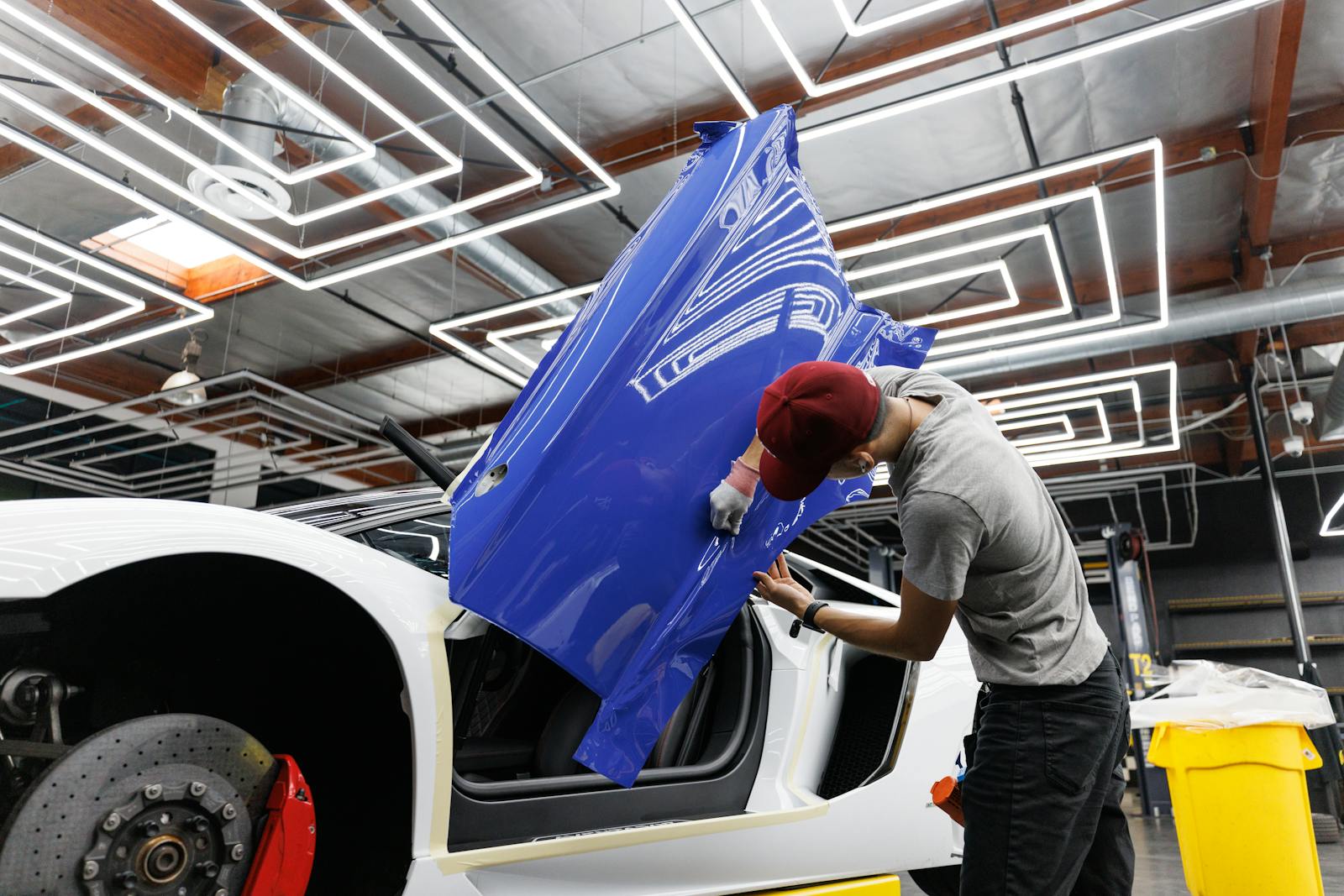 Auto mechanic applying blue vinyl wrap to a car door in a modern garage.