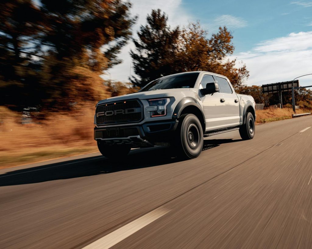 A Ford F-150 driving on a scenic highway surrounded by trees and blue skies.