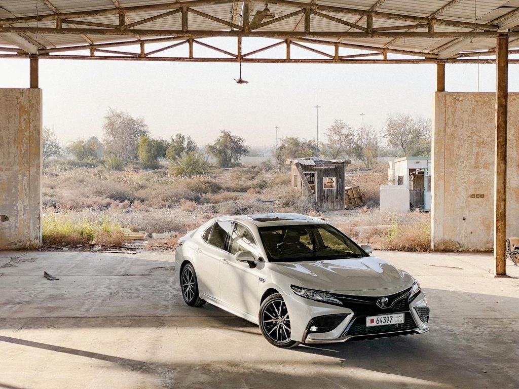 A white Toyota Camry elegantly parked in an industrial urban environment under a metal roof.