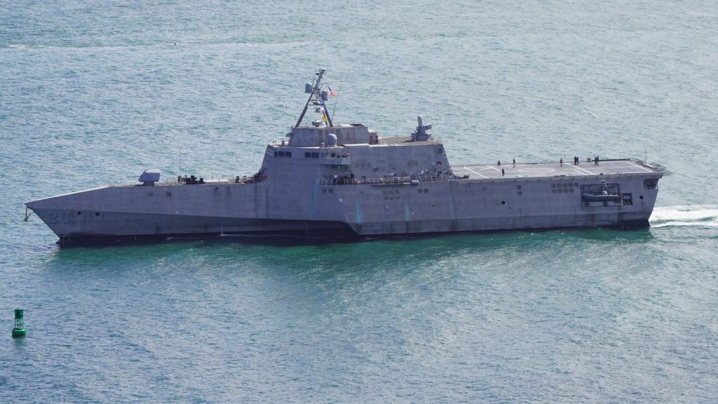 Aerial shot of a modern navy warship cruising through San Diego Bay under clear skies.