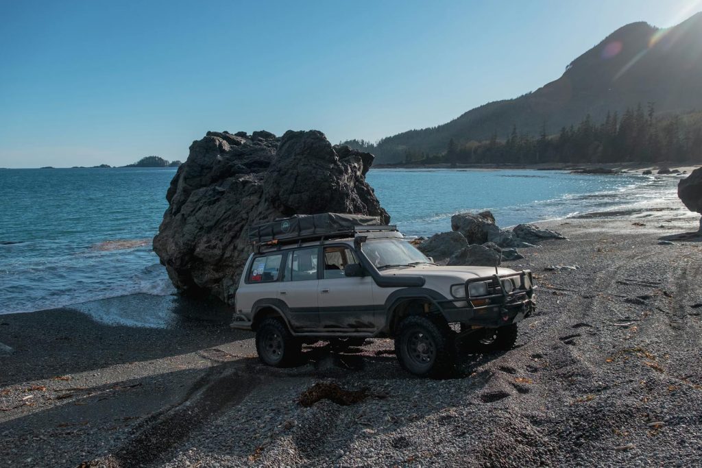 4x4 vehicle parked on a rocky beach near ocean waves, ideal for adventure themes.