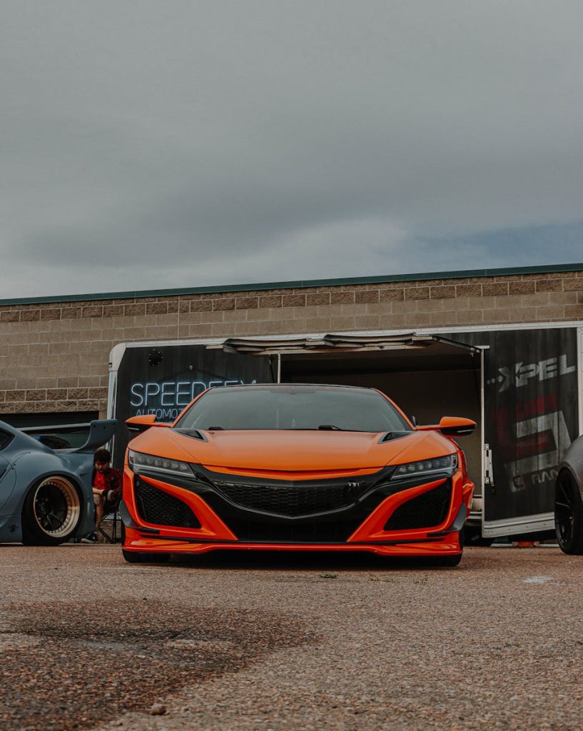 A sleek orange sports car prominently displayed outdoors at an auto show, ready for viewers.