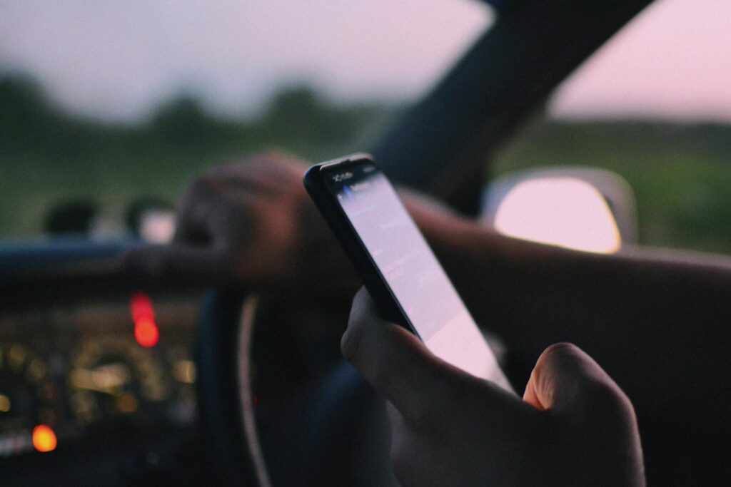 Close-up of a person using a smartphone while driving in a car at dusk.