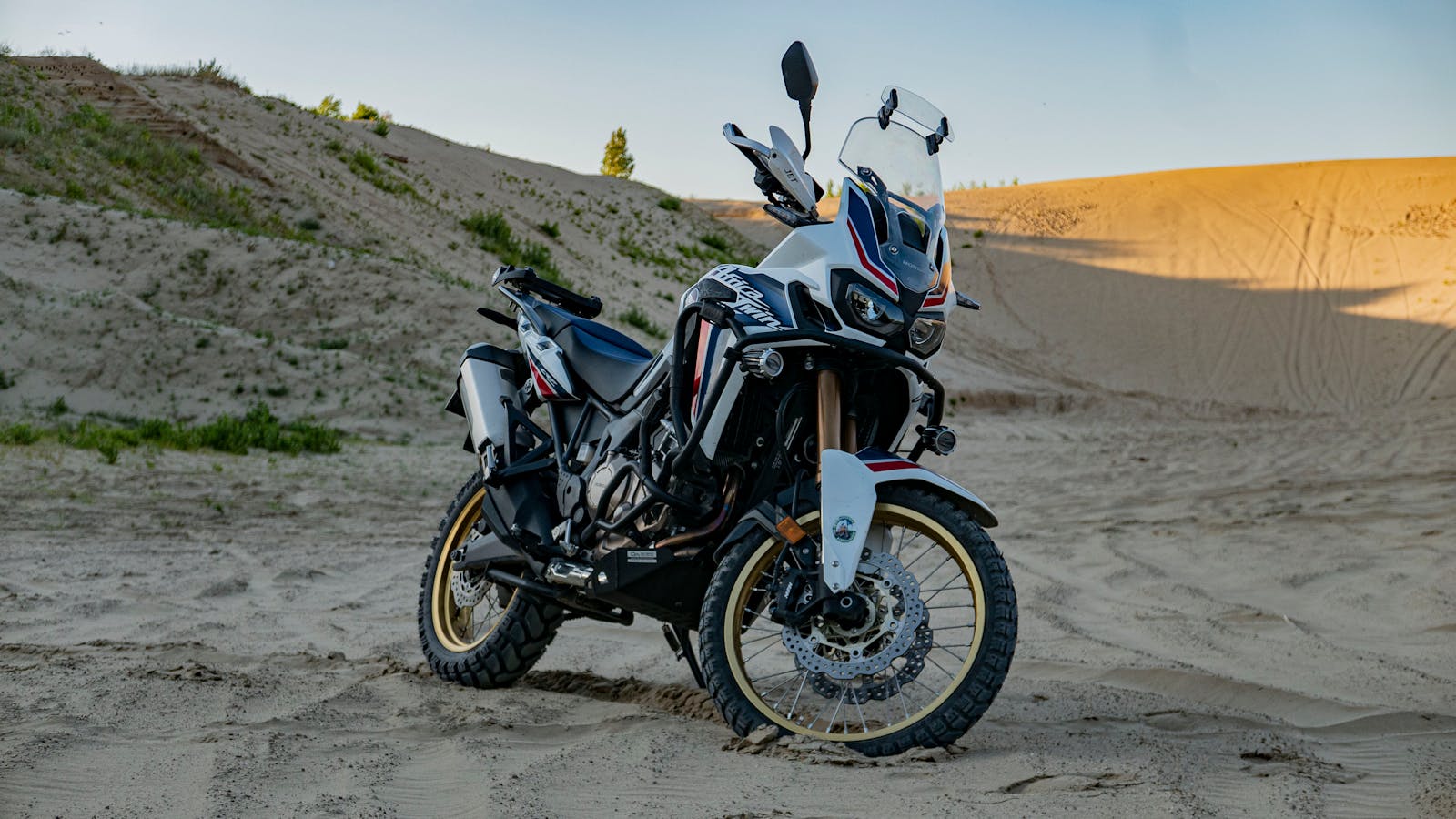 A rugged adventure motorcycle parked on expansive desert sand dunes, captured at daylight.