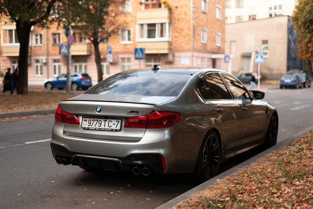 A stylish silver BMW M5 parked on a calm urban street in autumn.