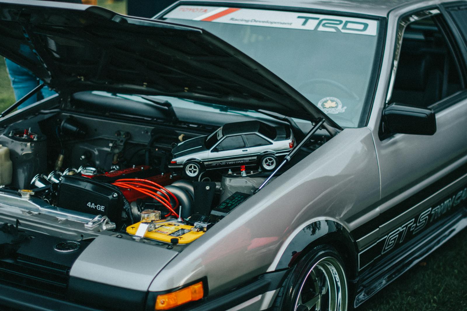 Detailed view of a car engine with hood open, showing intricate mechanical components and a car model on top.