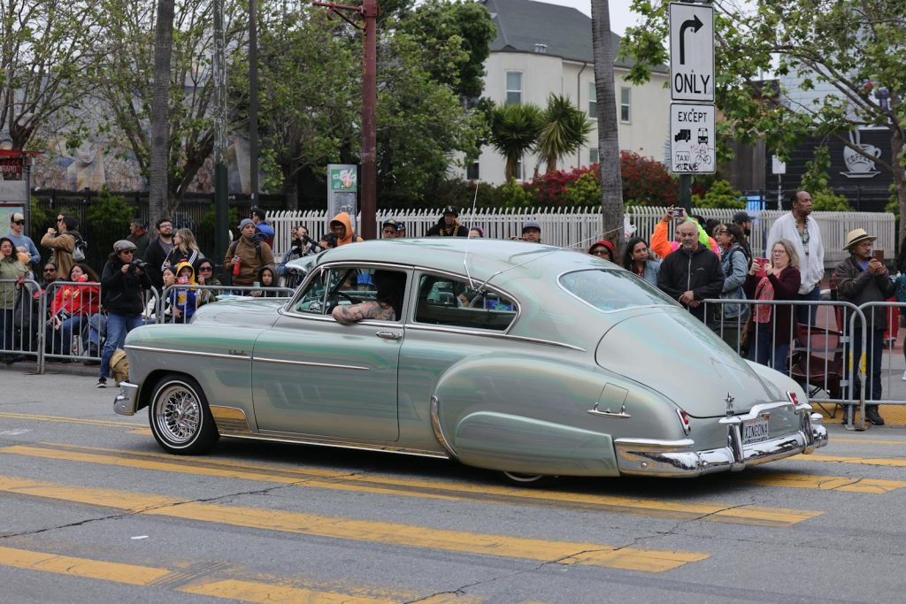 Vintage Chevrolet Fleetline lowrider showcased at a lively outdoor car show parade.
