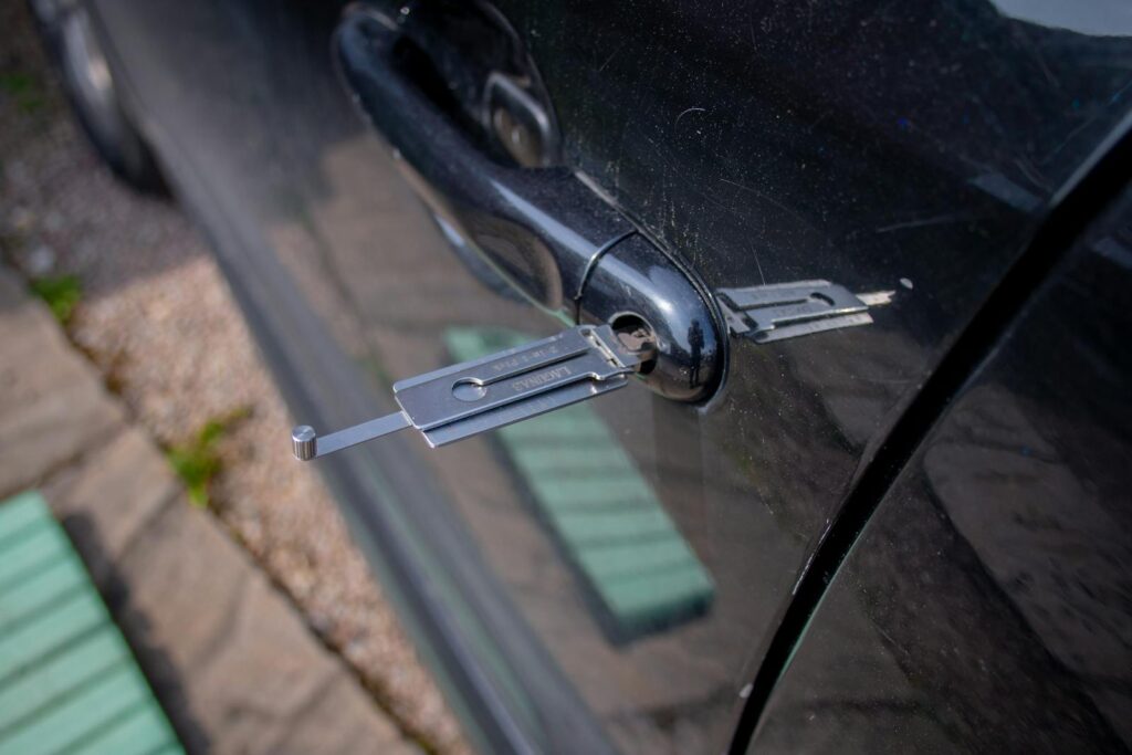 Close-up of a locksmith tool inserted into a car door lock, demonstrating security access.