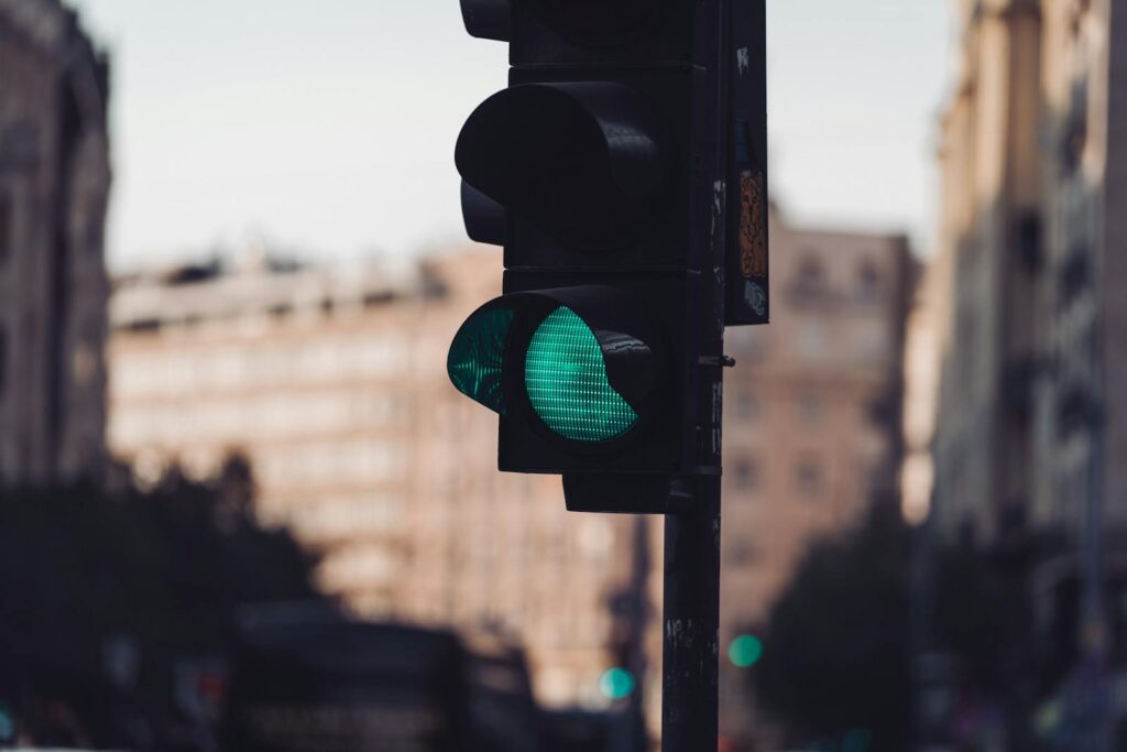 Green traffic light in an urban setting with blurred buildings in the background, conveying movement.