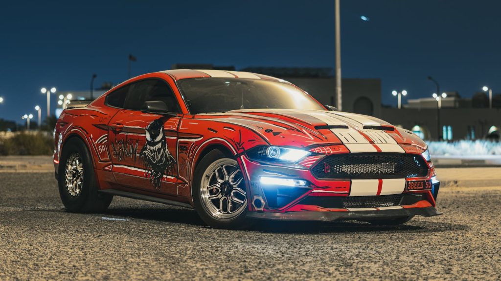 Custom Ford Mustang showcasing a striking red livery parked in an urban setting at night.