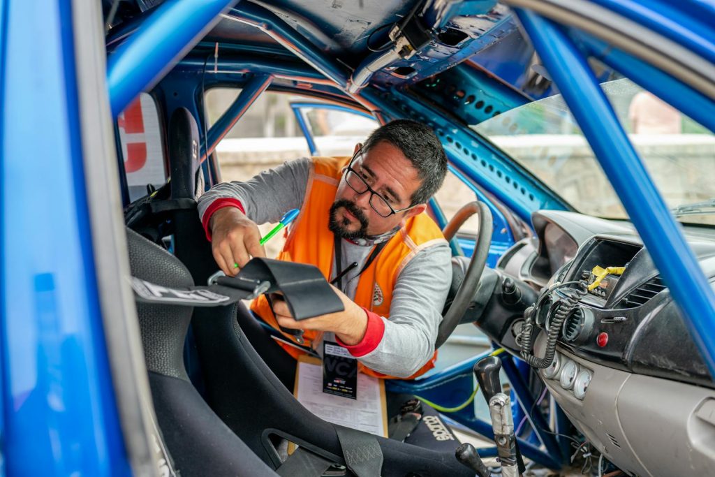 A racing car inspector with eyeglasses checks interior components and safety features in a blue race car.