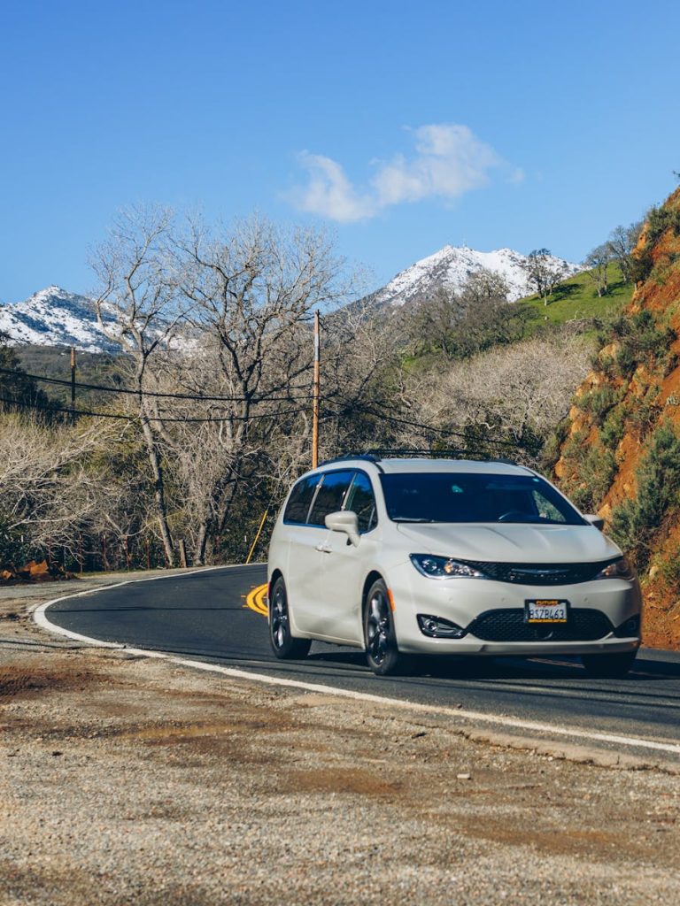 Minivan driving along a winding mountain road with snowcapped peaks.