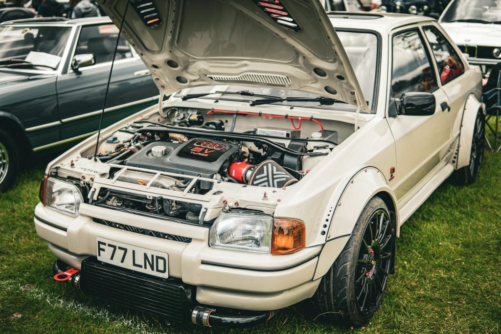 Customized rally car with open hood showcasing engine at a car gathering.