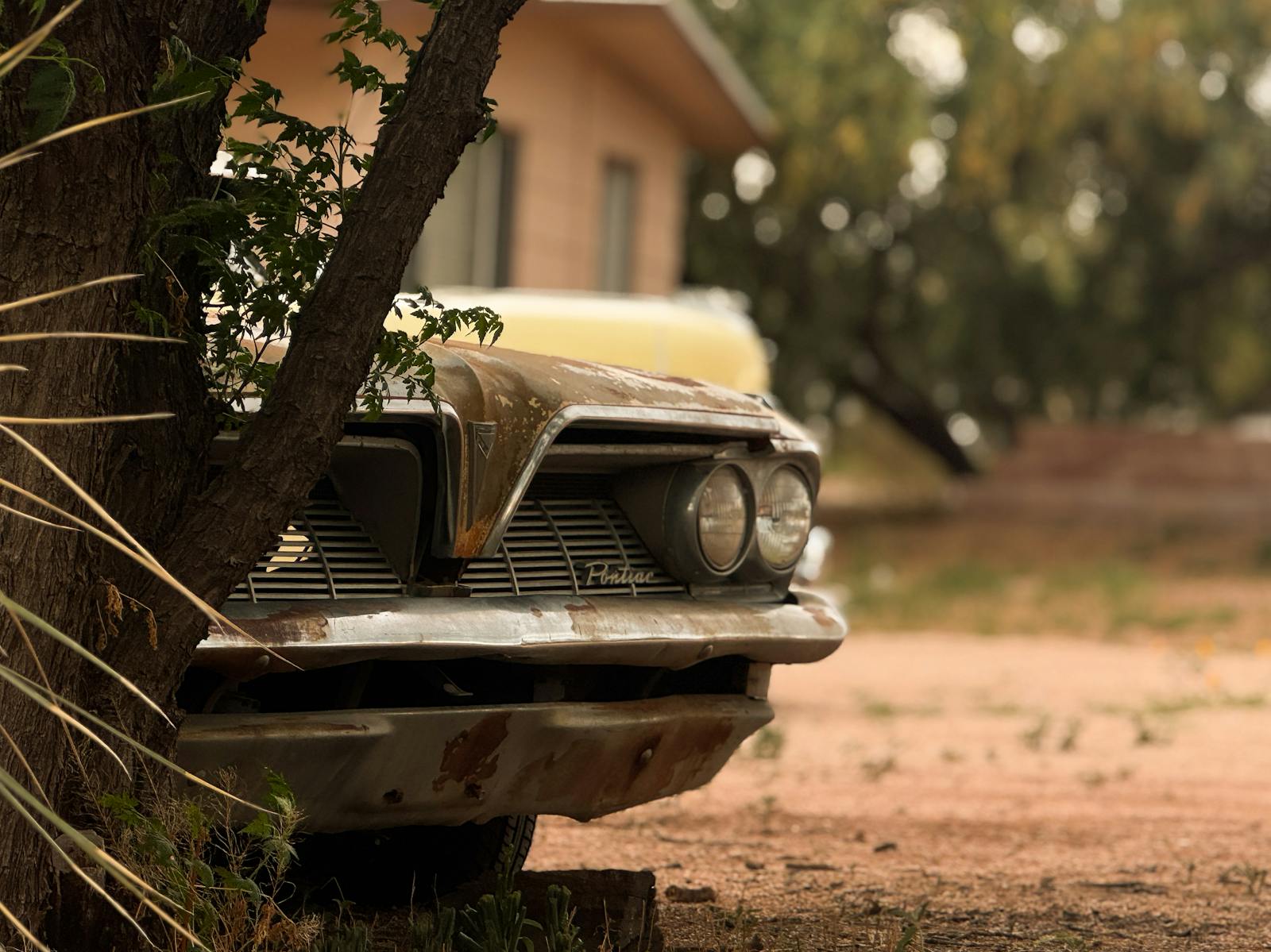 Abandoned classic Pontiac car with rust in a dry, desert setting.