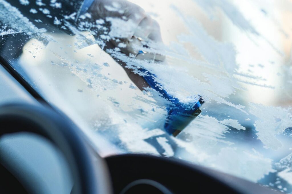 Hand scraping ice off a car windshield during a cold winter morning.