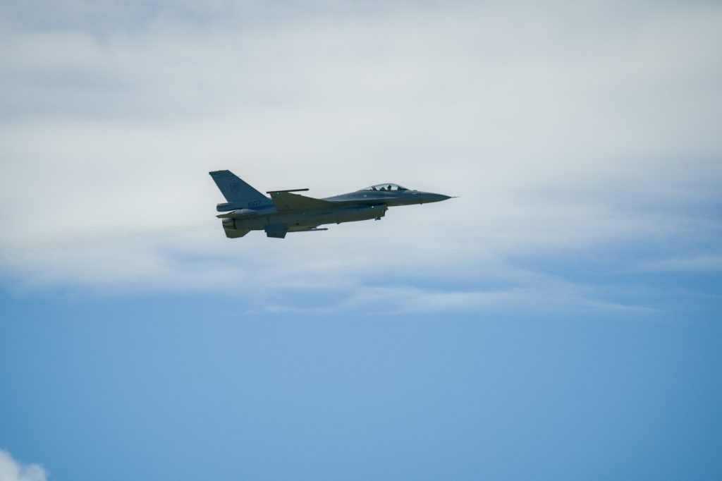 A fighter jet flies through a cloudy blue sky