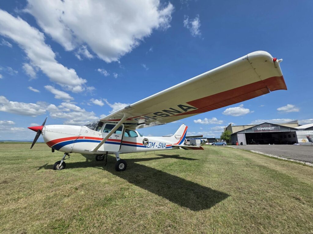 A light aircraft parked on a clear day near a hangar at an airport, showcasing aviation design.