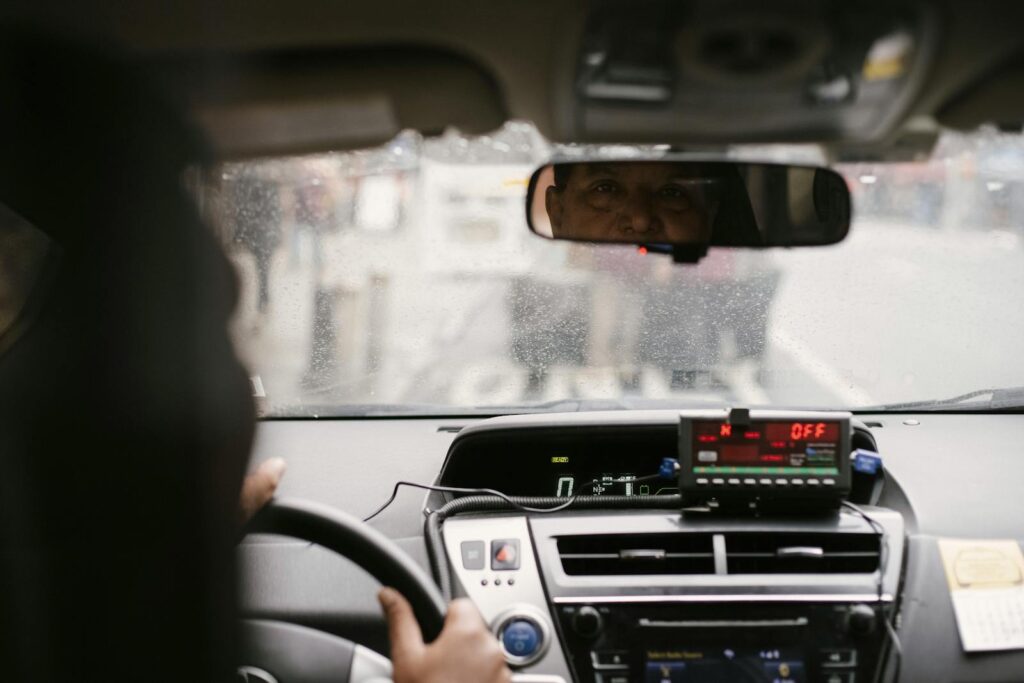 Back view of man reflecting in mirror while driving along street in city on urban background in soft daylight