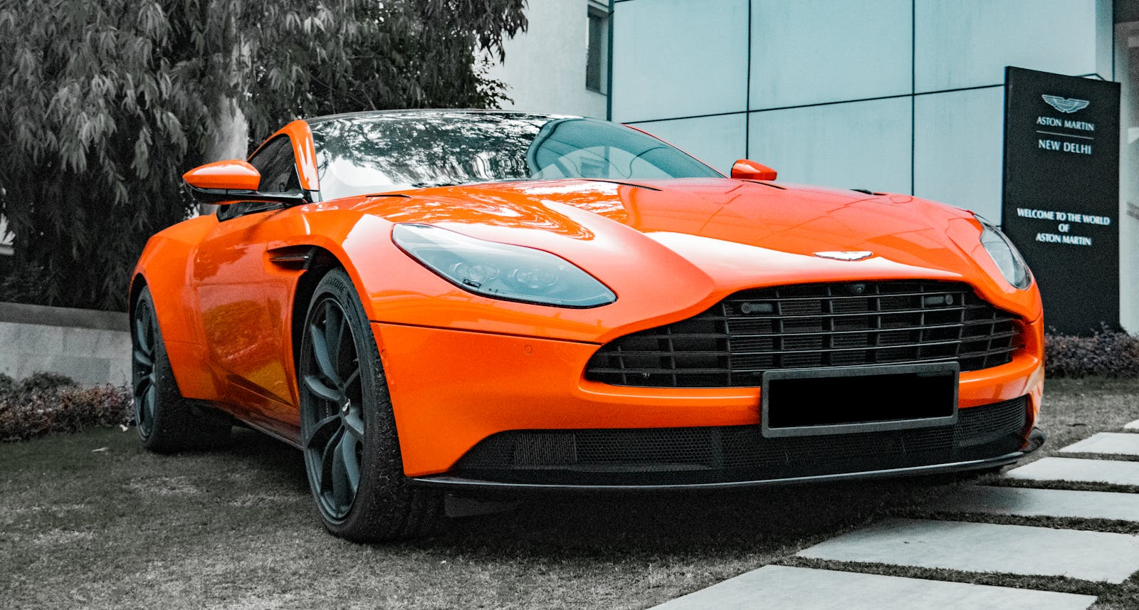Stunning orange Aston Martin DB11 parked outside showroom in New Delhi.