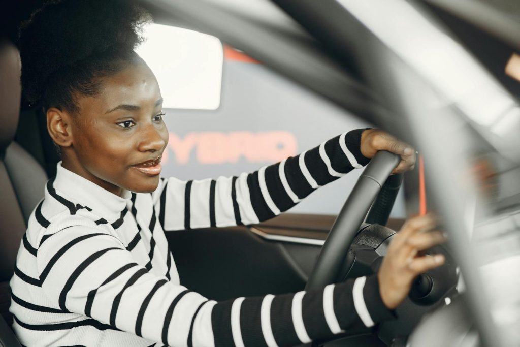 African American woman driving a car, smiling and confident behind the wheel from interior view.