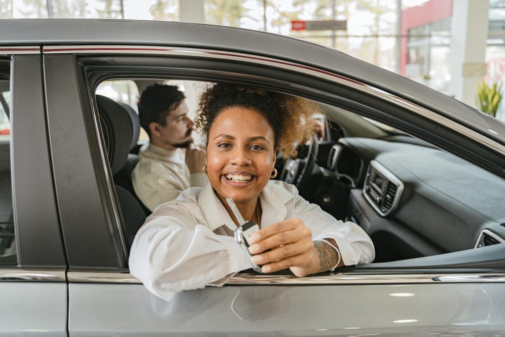 Joyful couple in their new car, holding keys in a dealership showroom, smiling warmly.