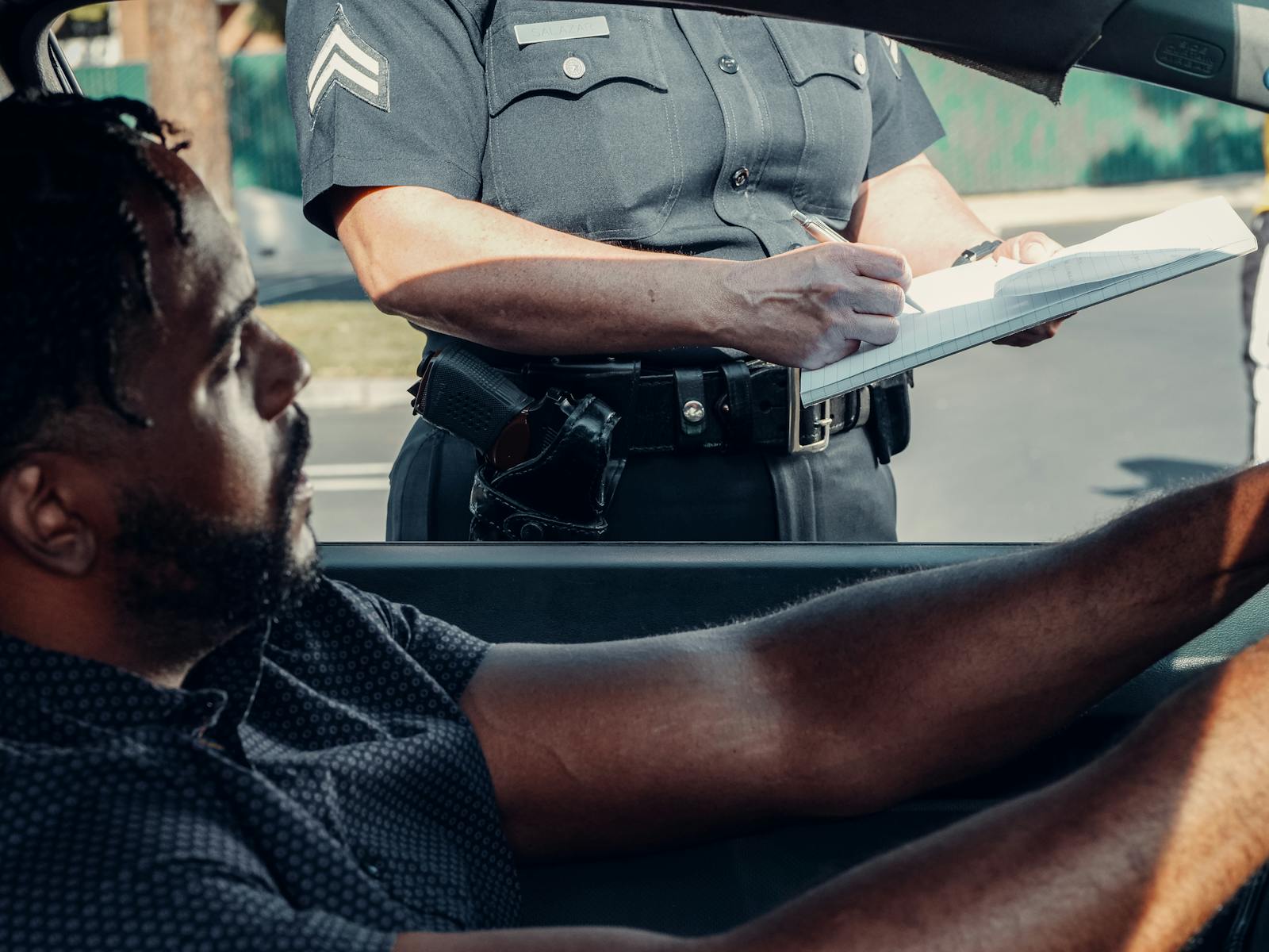 A police officer issues a traffic ticket to a driver seated in a car during the day.