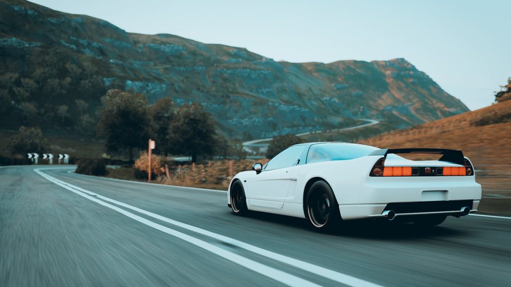 A sleek white sports car speeding through a scenic mountain road during the day.