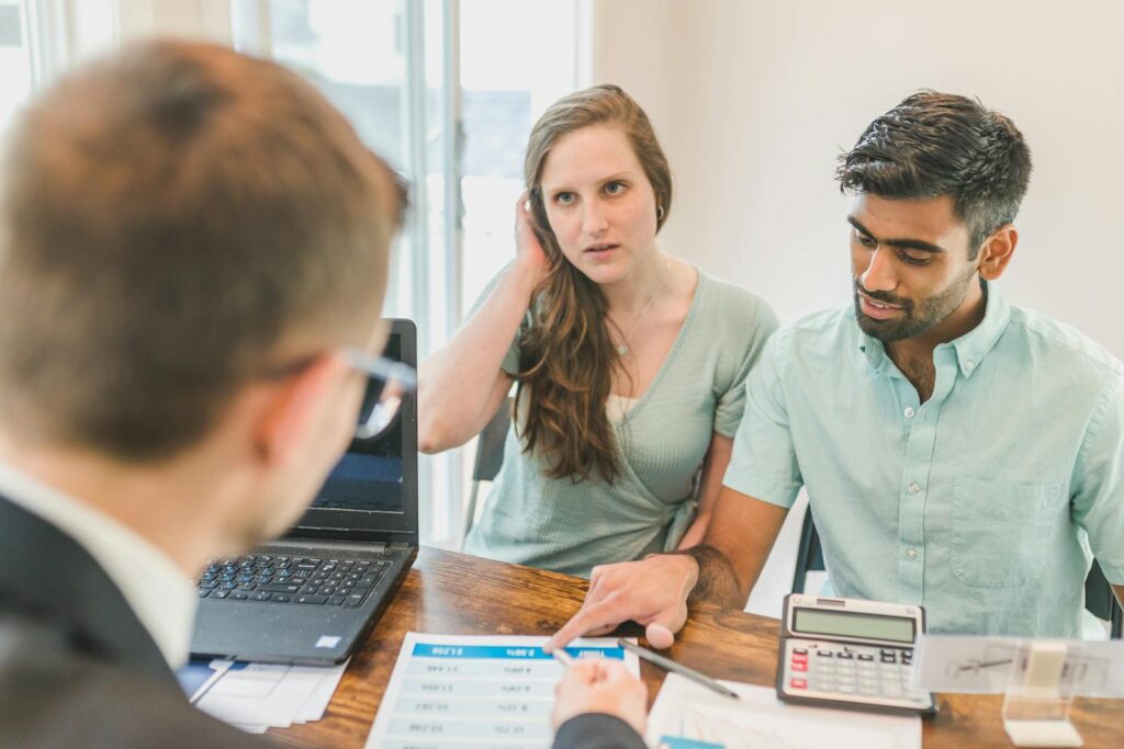 A young couple consults with a realtor about buying a home, indoors in a modern office setting.
