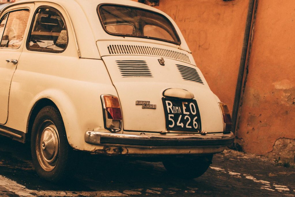 A classic Fiat 500 parked on a cobblestone street in Rome with a vintage feel.