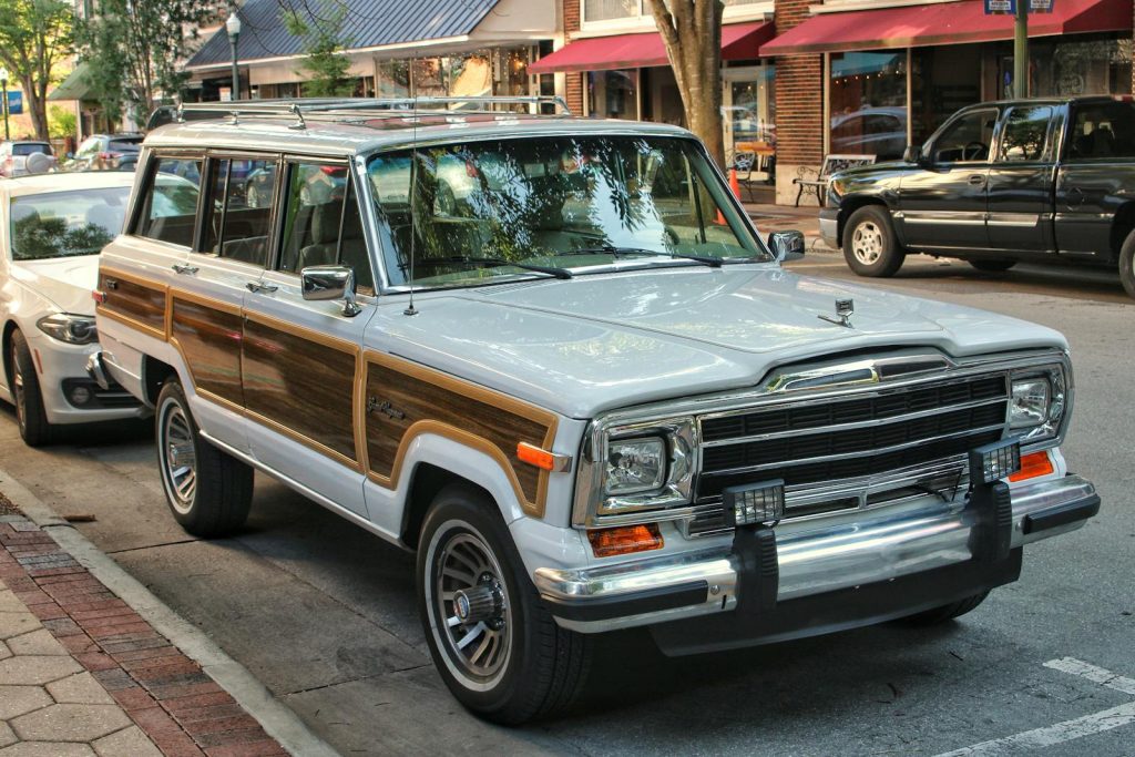 Classic Jeep Wagoneer with wood paneling parked on an urban street, reflecting a vintage aesthetic.