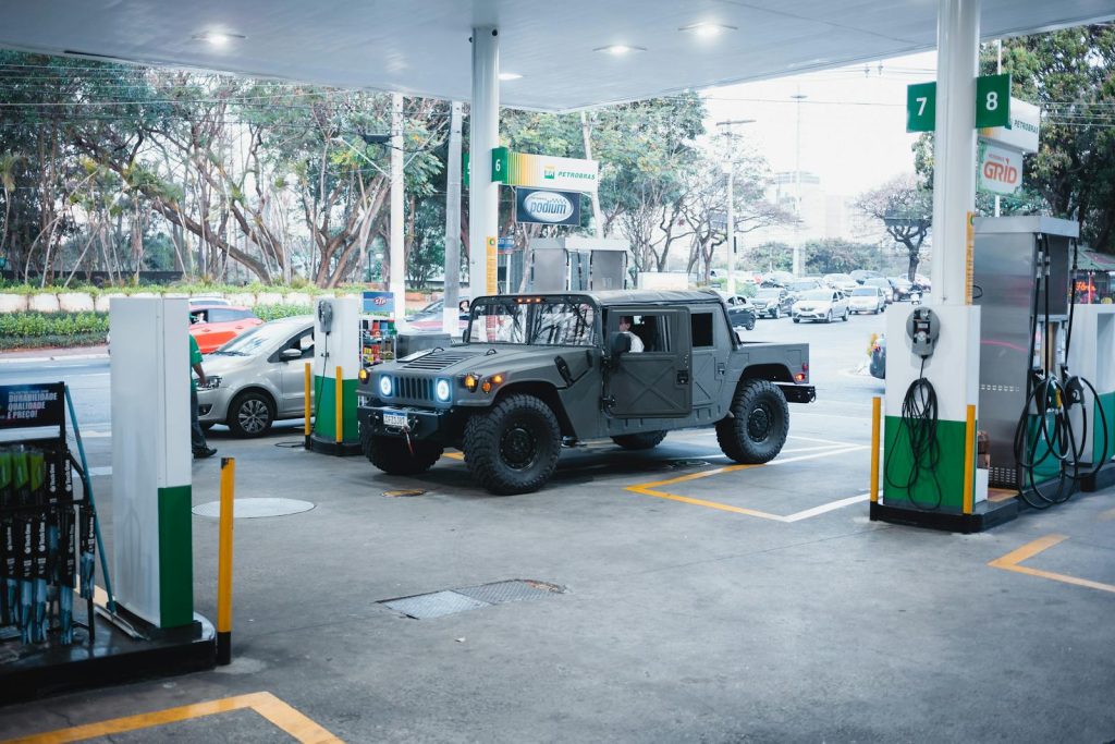 A rugged Hummer H1 parked at a busy gas station in an urban setting.