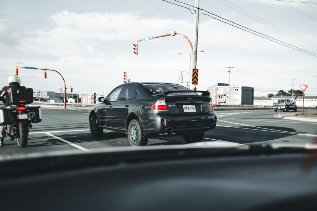 A motorcycle and car wait at a busy city intersection under traffic lights.