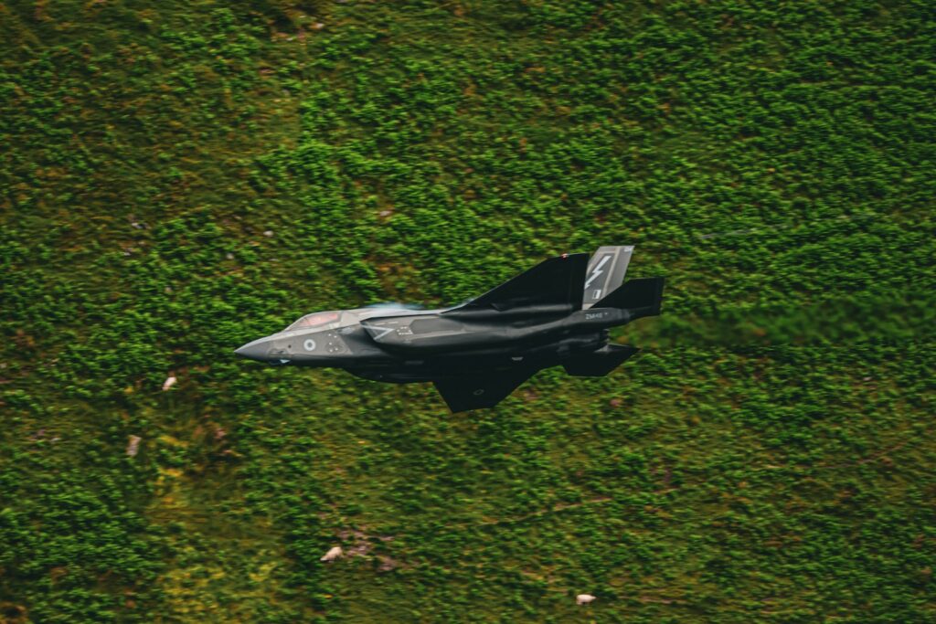 A fighter jet flying over a lush green field