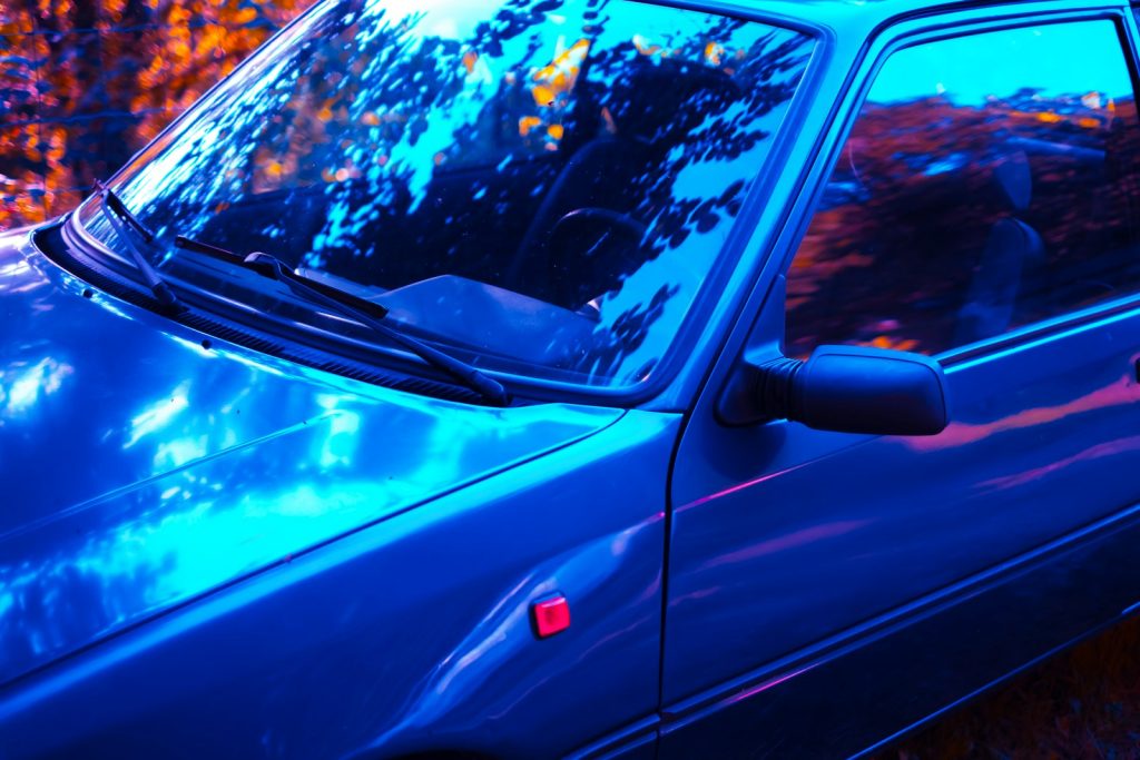 Blue car with reflections of trees at dusk