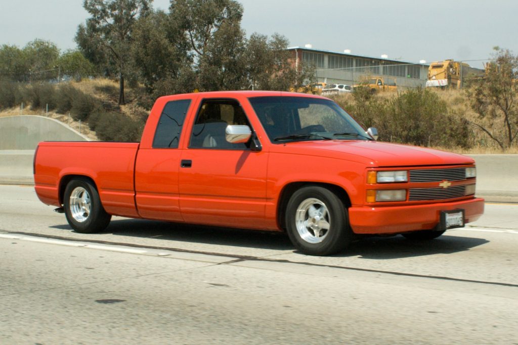 A bright orange pickup truck driving on a highway.