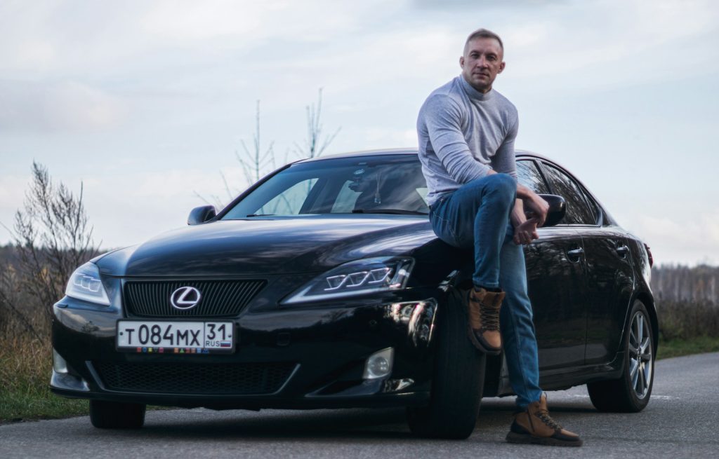 Man leaning on a black lexus sedan outdoors.