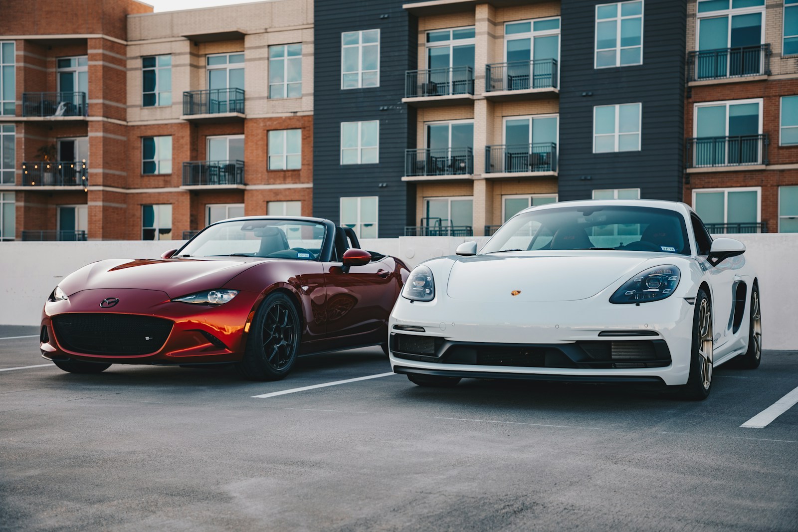Two sports cars parked in front of an apartment.