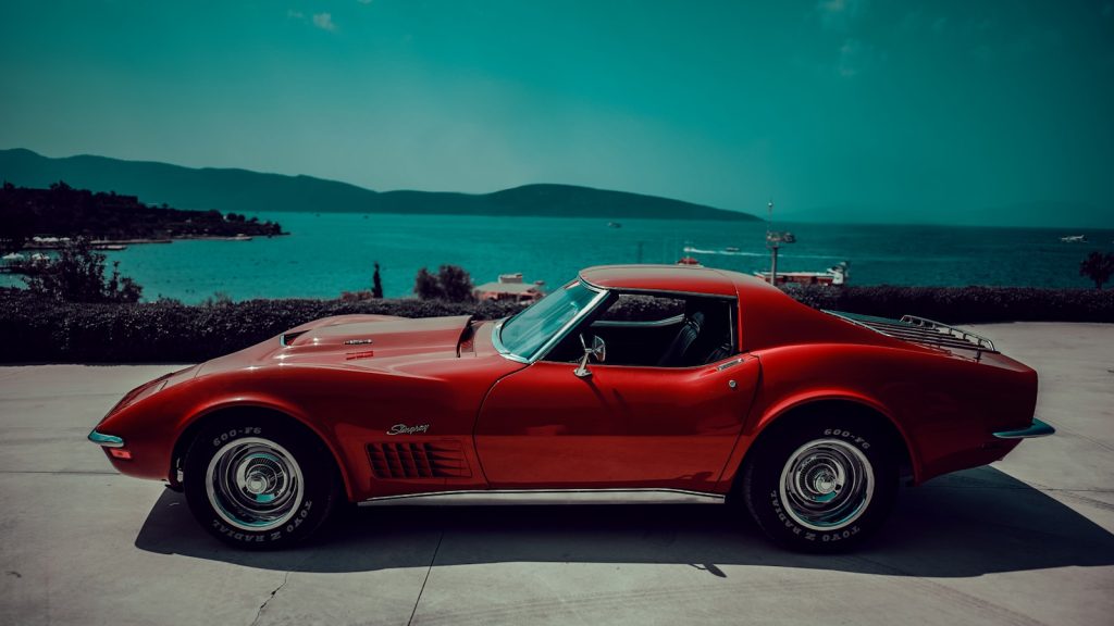 Red vintage car parked by the blue ocean.