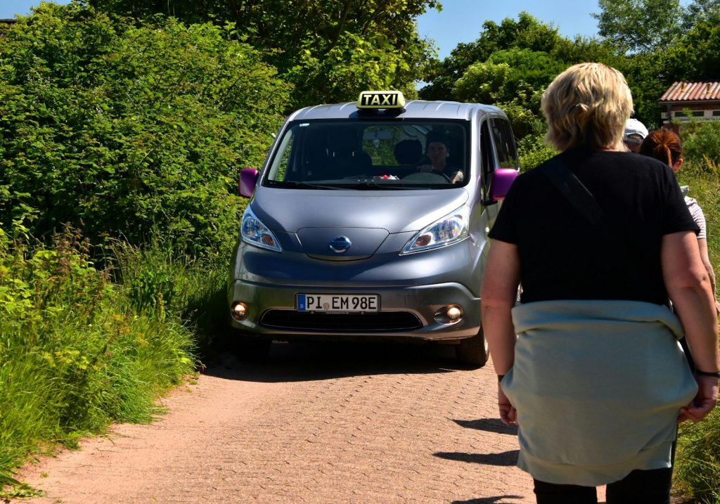 A woman walking down a dirt road next to a car
